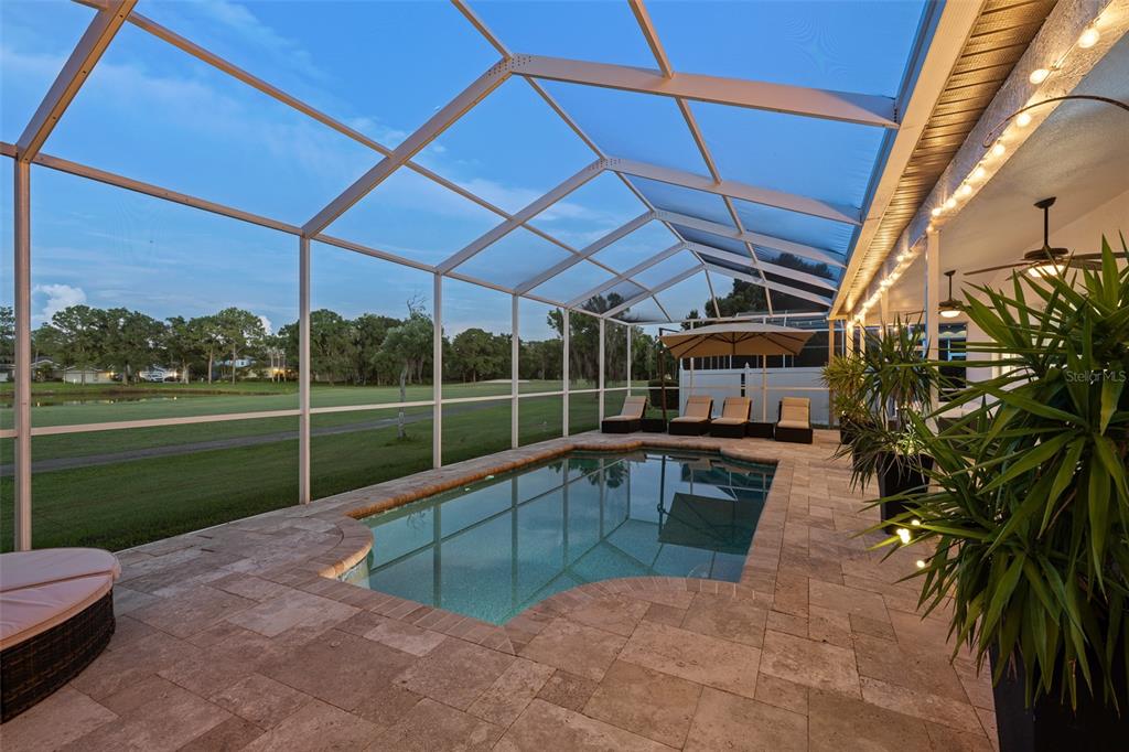 A screened-in pool patio features stone pavers, lounge chairs, and a view of a golf course — 15615 SHOAL CREEK PLACE, ODESSA, FL