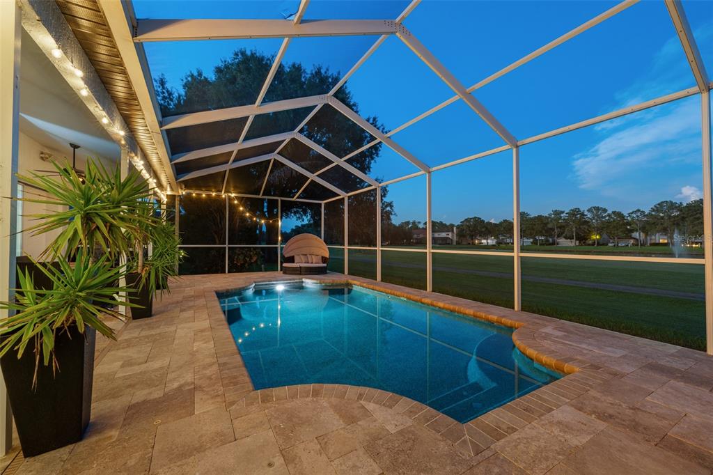 A screened-in pool patio features stone pavers, string lights, and a view of a golf course — 15615 SHOAL CREEK PLACE, ODESSA, FL