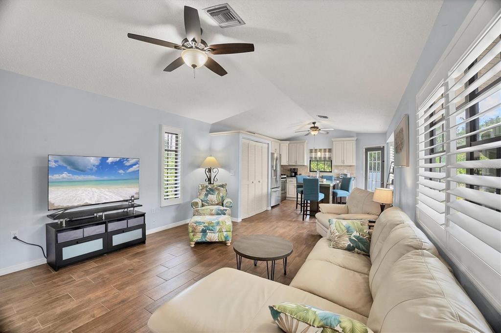 A living room with a beige sectional, floral armchair, television, and an open-concept kitchen area — 255 BOUNDARY BOULEVARD UNIT 105, ROTONDA WEST, FL
