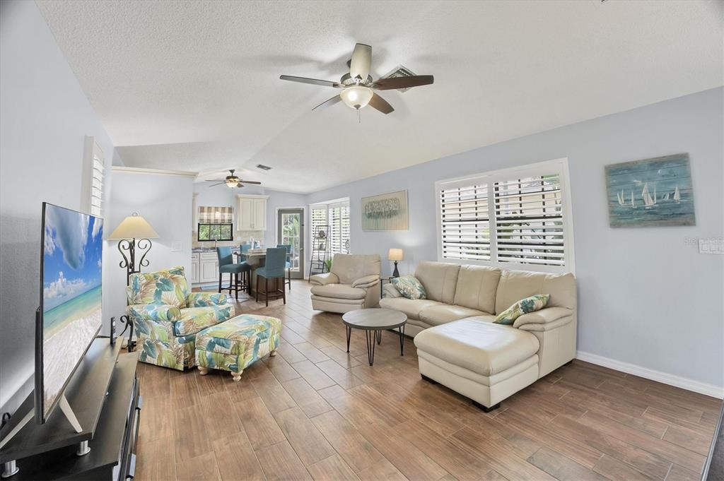 A living room with tile floors, a beige sectional, a floral armchair, and a kitchen area — 255 BOUNDARY BOULEVARD UNIT 105, ROTONDA WEST, FL