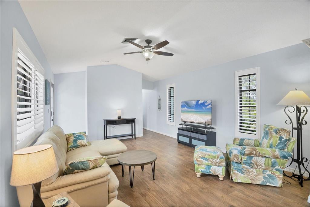 A living room features light blue walls, wood-look flooring, a sectional sofa, and a television — 255 BOUNDARY BOULEVARD UNIT 105, ROTONDA WEST, FL