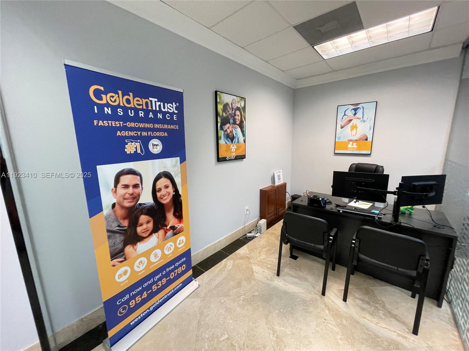 An office space features a large promotional banner, a desk with two chairs, and wall art — 2893 Executive Park Dr # 104, Weston FL 33331, WESTON, FL