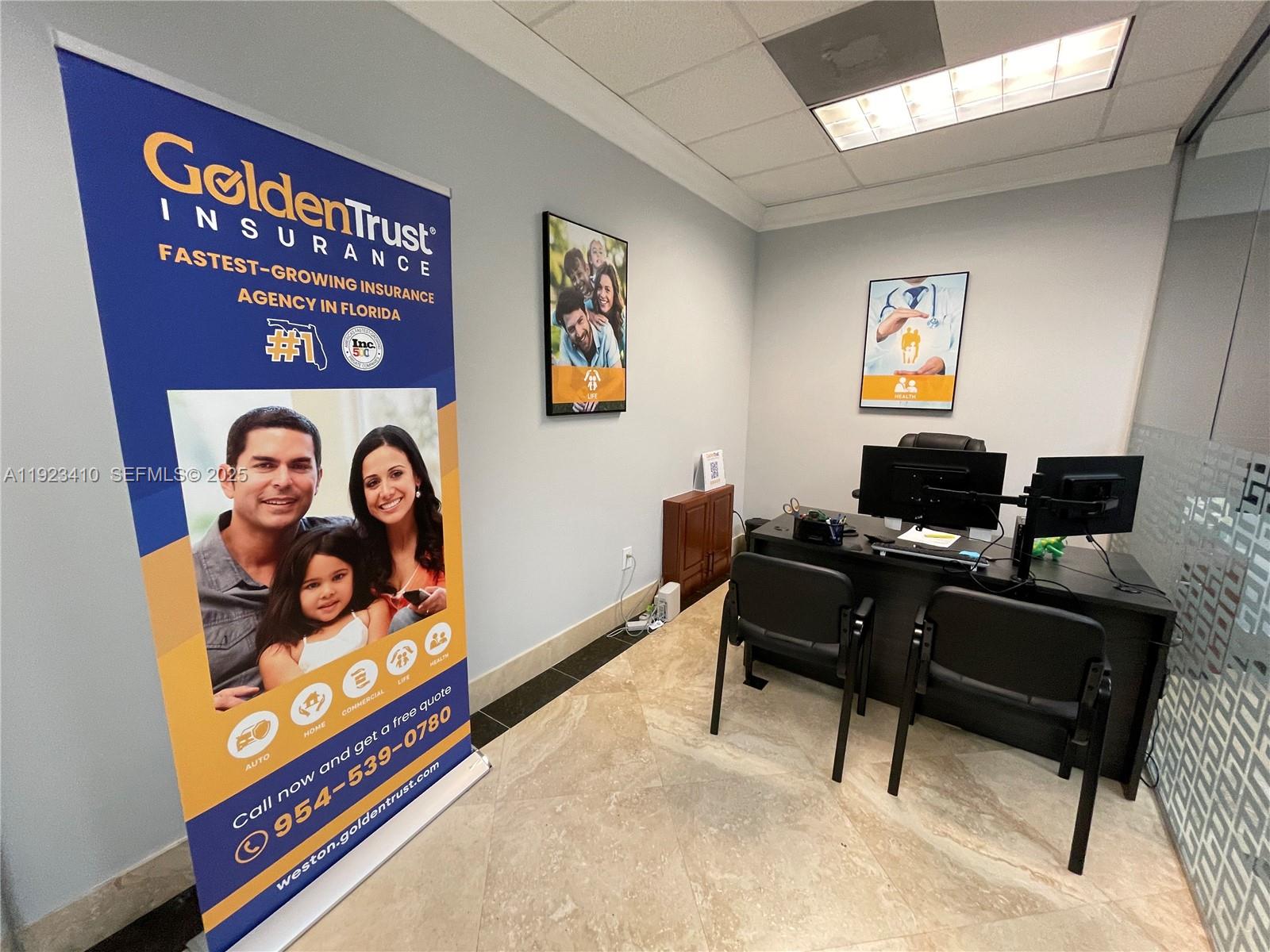 An office space features a branded banner, a desk with two chairs, and wall art — 2893 Executive Park Dr # 104, Weston FL 33331, WESTON, FL