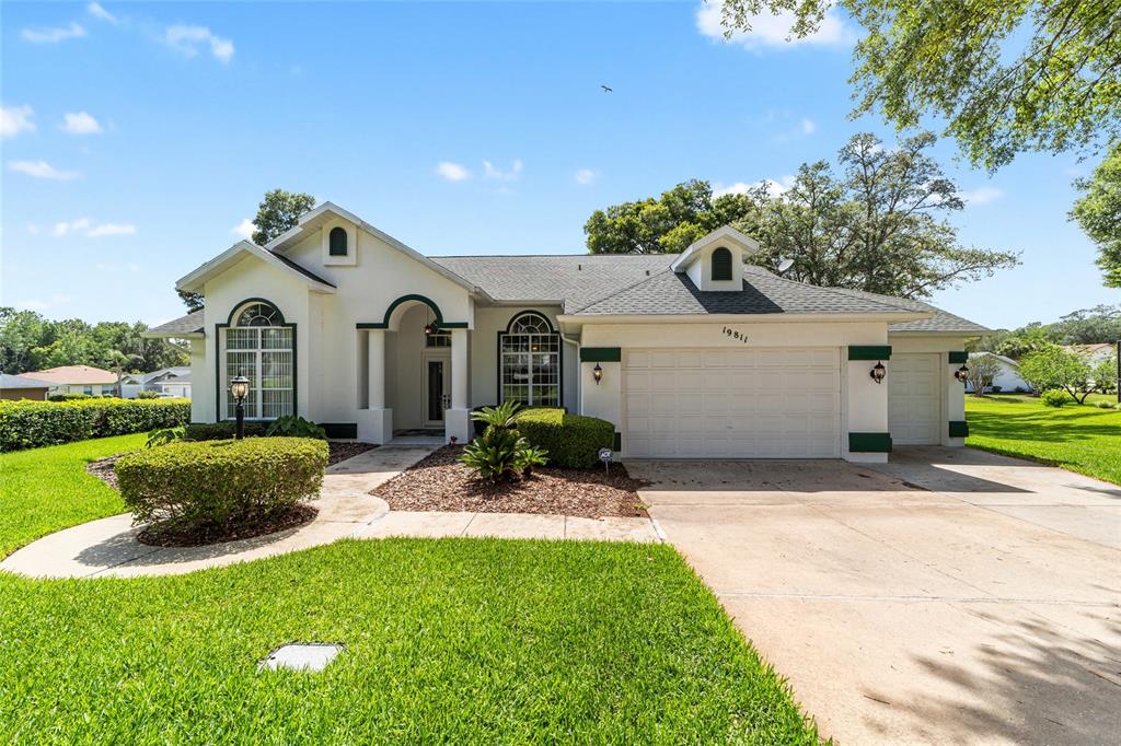 A single-story house with a white exterior, green trim, and a two-car garage — 19811 SW 95TH STREET, DUNNELLON, FL