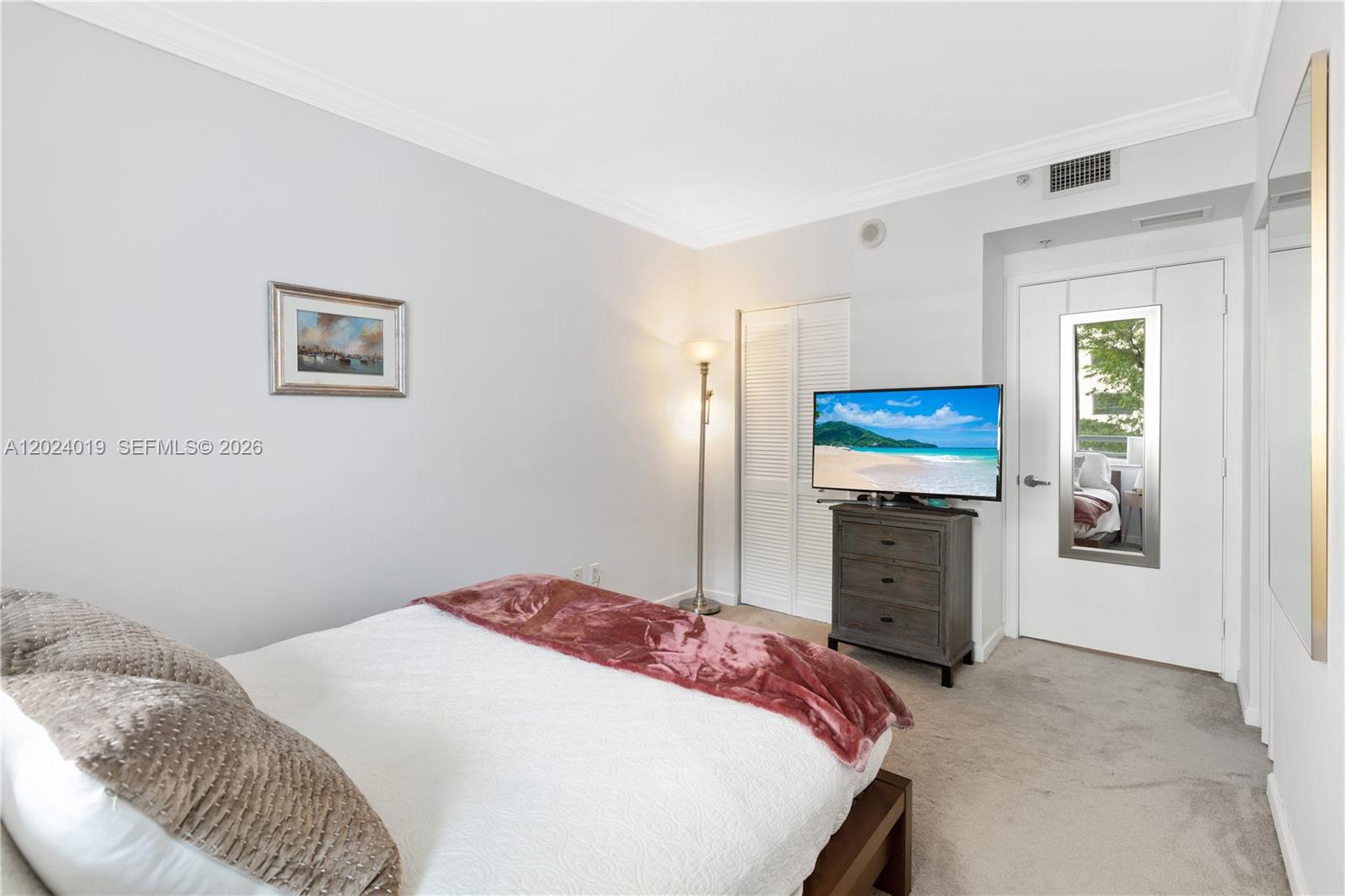 A bedroom features a bed, a television on a dresser, and a mirrored door — 335 S Biscayne Blvd # 802, Miami FL 33131, MIAMI, FL