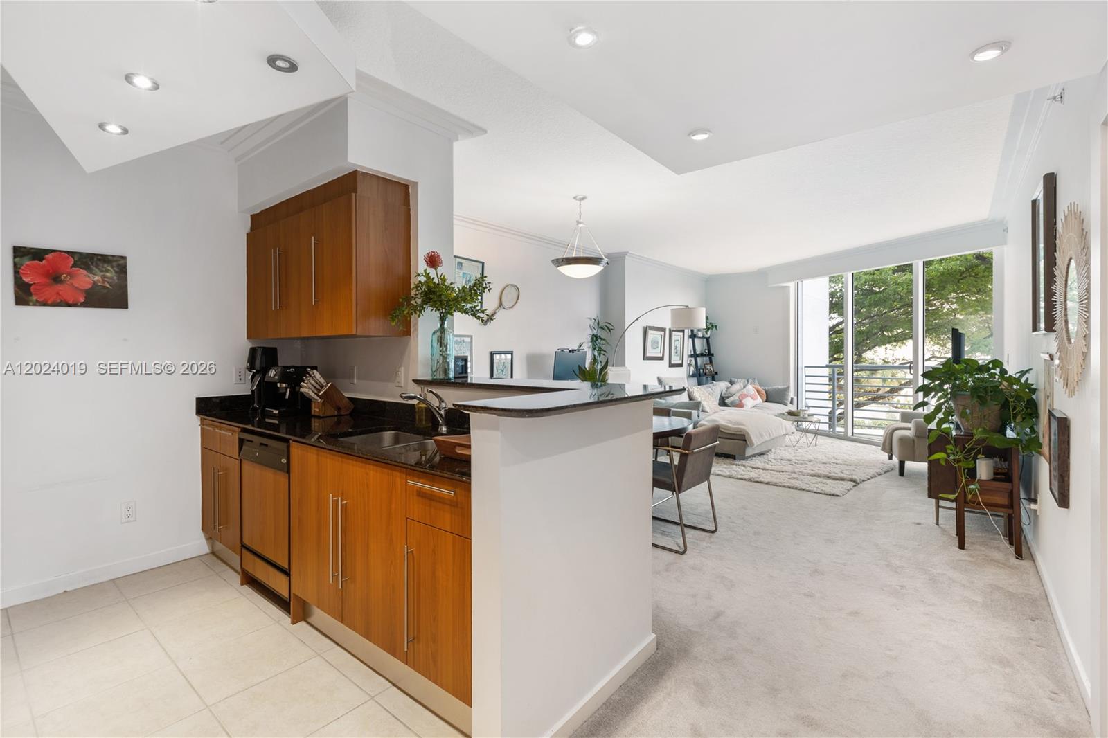 A kitchen with wood cabinets and black countertops opens into a carpeted living area — 335 S Biscayne Blvd # 802, Miami FL 33131, MIAMI, FL