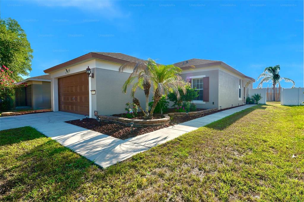 A single-story house with a brown garage door, tan stucco walls, and a palm tree — 1072 HILL FLOWER DRIVE, BROOKSVILLE, FL