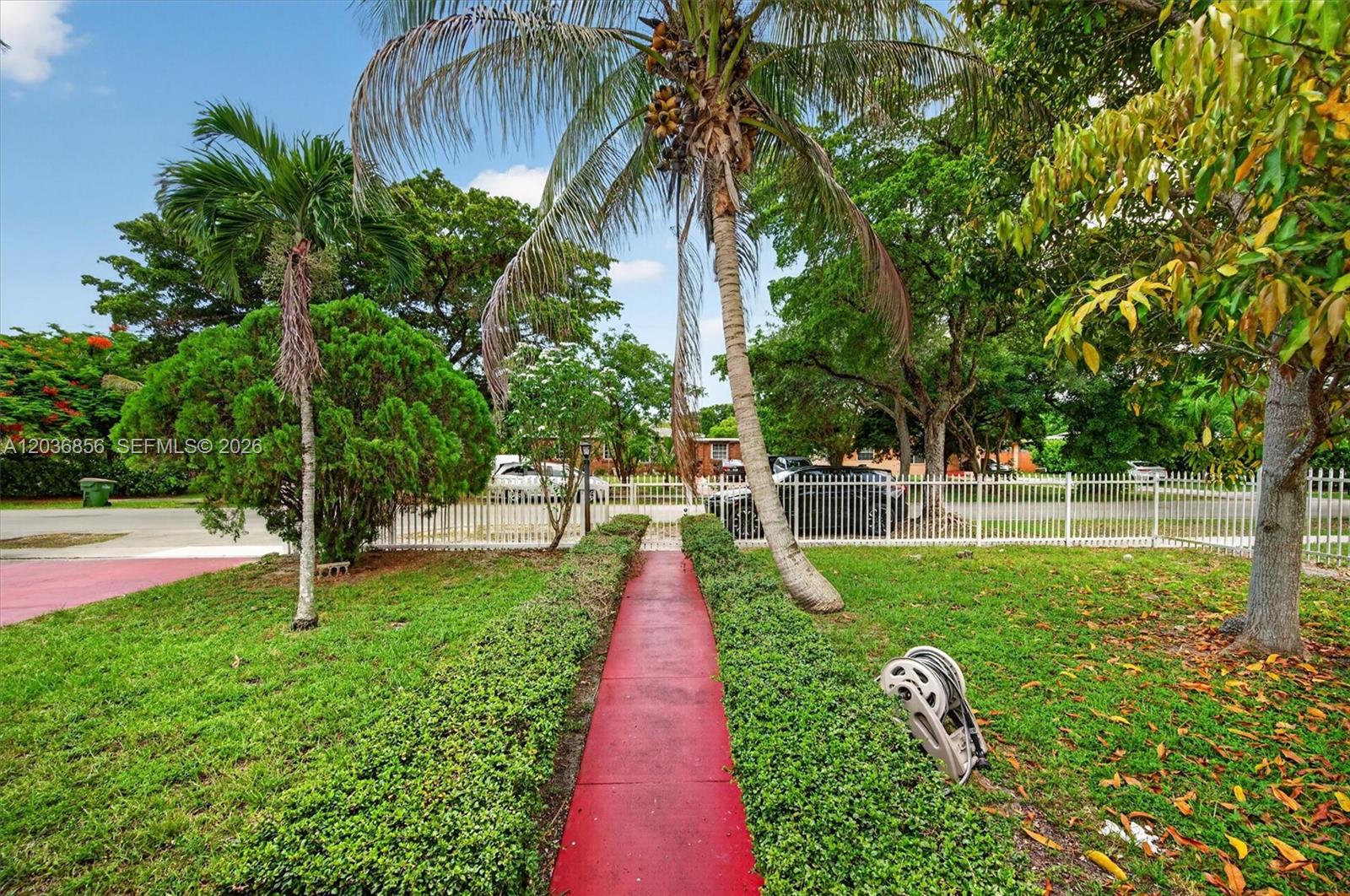 A red walkway leads through a grassy front yard toward a white fence and trees — 761 NE 139th St, North Miami FL 33161, NORTH MIAMI, FL