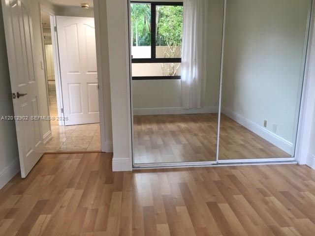 A room with light wood flooring, a mirrored closet, and a white door leading elsewhere — 151 Crandon Blvd # 128, Key Biscayne FL 33149, KEY BISCAYNE, FL