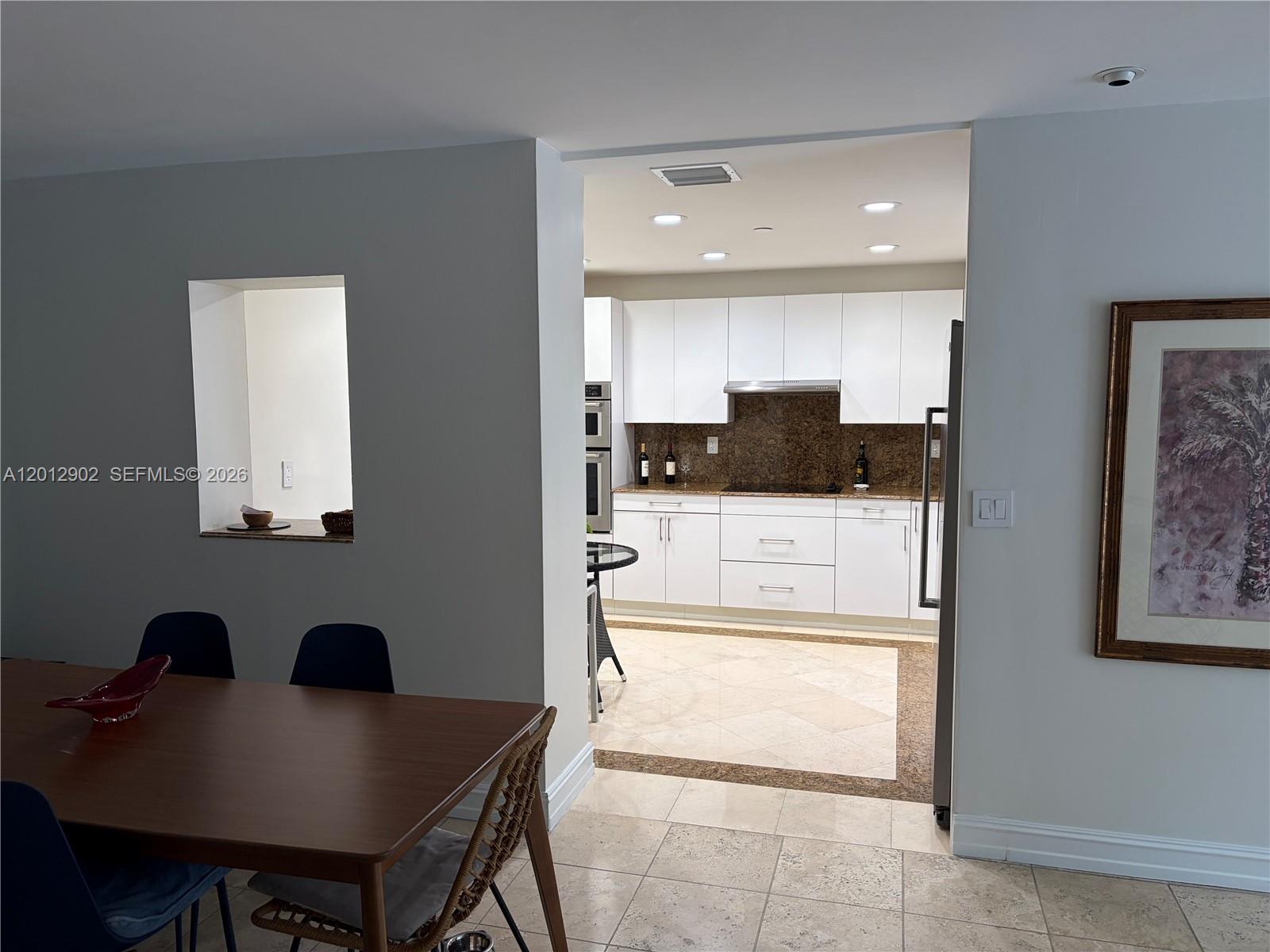 A dining area opens into a kitchen with white cabinets and stone countertops — 151 Crandon Blvd # 128, Key Biscayne FL 33149, KEY BISCAYNE, FL