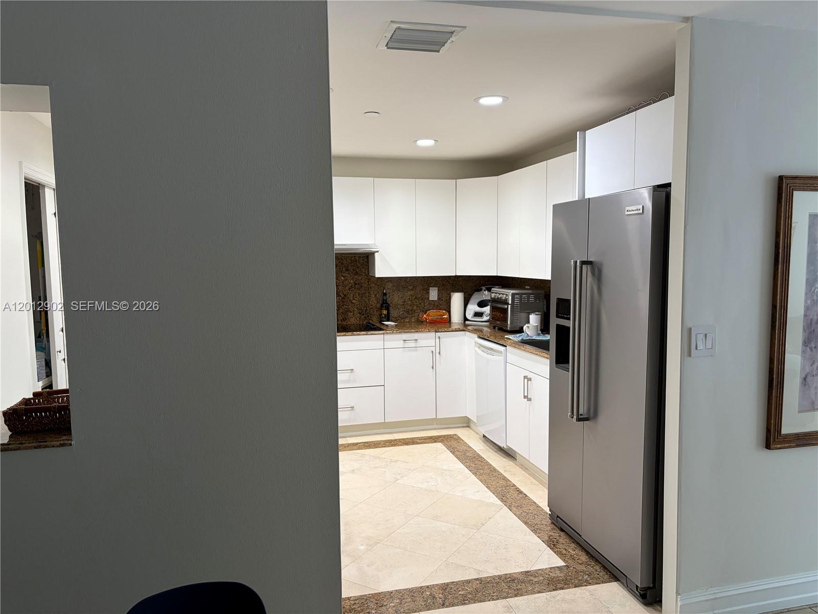 A kitchen features white cabinets, stainless steel appliances, and a stone-tiled floor with a border — 151 Crandon Blvd # 128, Key Biscayne FL 33149, KEY BISCAYNE, FL