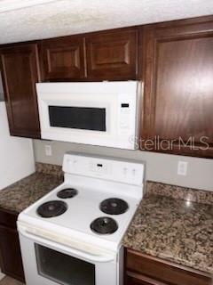 A kitchen features dark wood cabinets, a white microwave, and a white electric stove — 900 LAKE DESTINY ROAD UNIT B, ALTAMONTE SPRINGS, FL