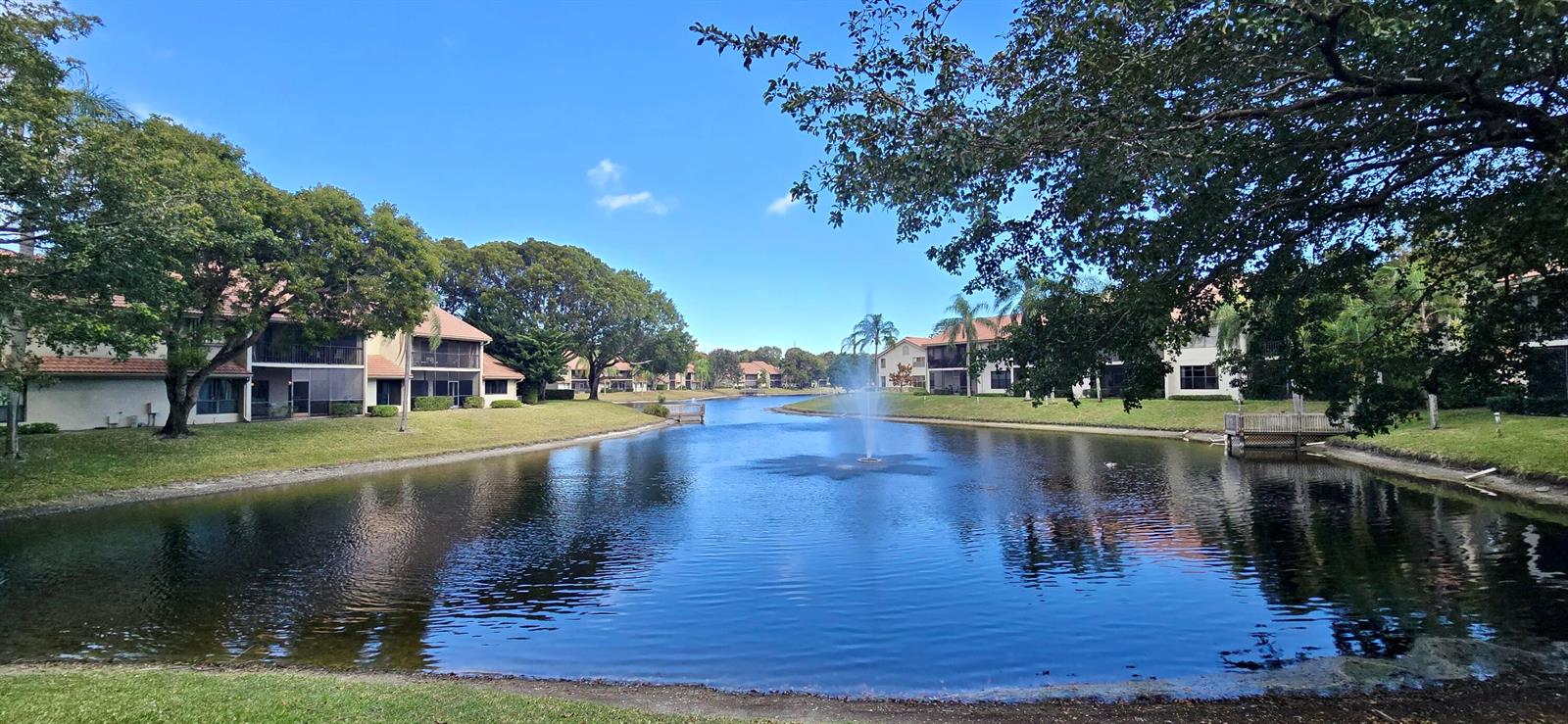 A pond with a central fountain sits between multi-story apartment buildings and green lawns — 5521 Coach House Circle # D, Boca Raton FL 33486, BOCA RATON, FL
