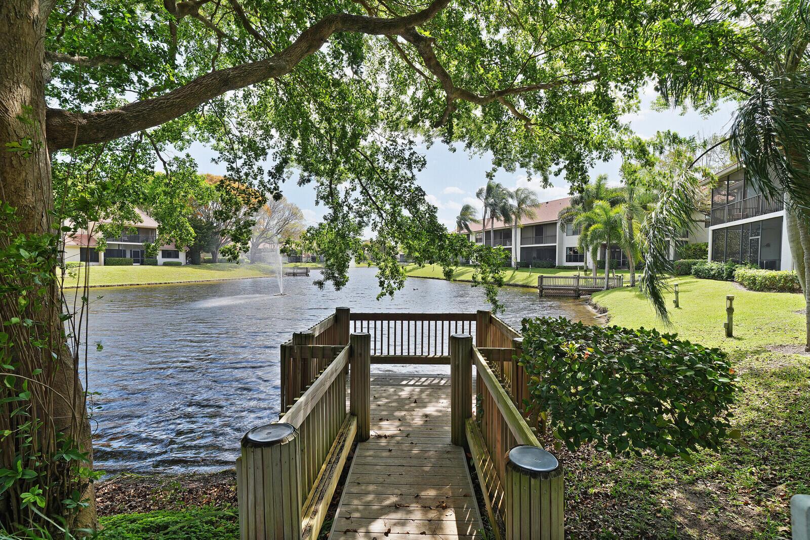 A wooden dock extends over a lake surrounded by apartment buildings and large trees — 5521 Coach House Circle # D, Boca Raton FL 33486, BOCA RATON, FL