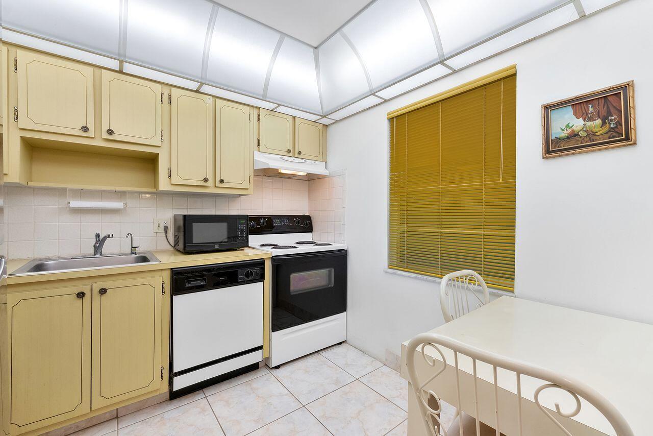 A kitchen with yellow cabinets, white appliances, a tiled floor, and a small dining table — 7807 Golf Cir Drive # 308, Margate FL 33063, MARGATE, FL