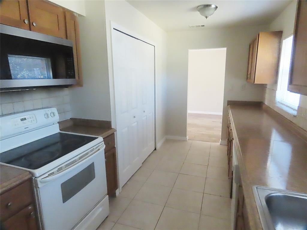 A kitchen features white appliances, wood cabinets, tan countertops, and light-colored tile flooring — 749 SEMINOLE AVENUE, LONGWOOD, FL