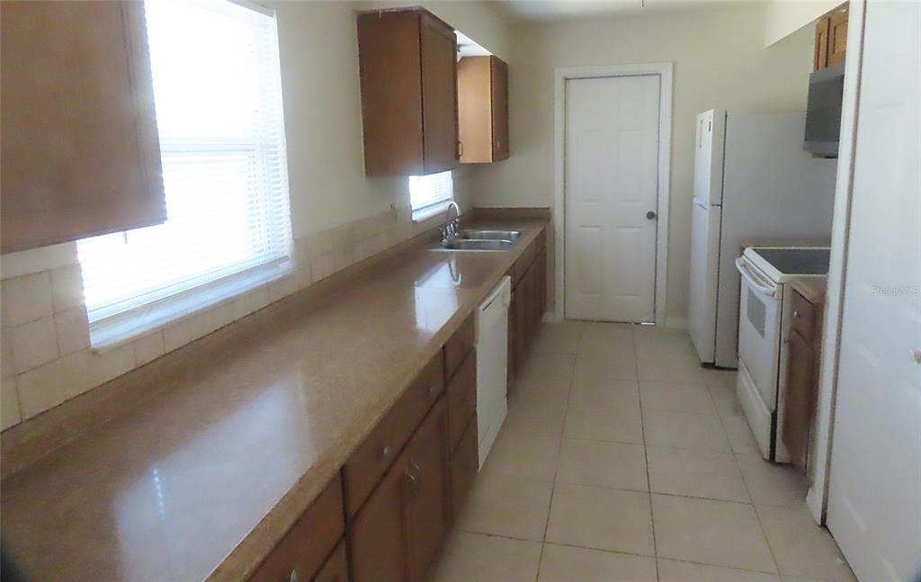 A kitchen features wood cabinets, a long countertop, a white dishwasher, and a white refrigerator — 749 SEMINOLE AVENUE, LONGWOOD, FL