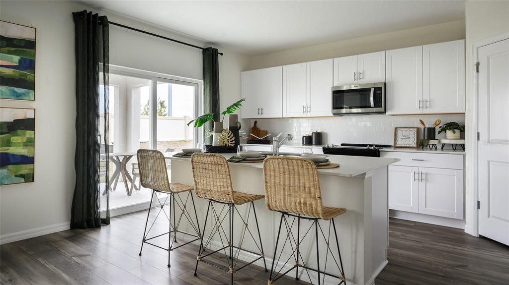 A modern kitchen features white cabinets, a central island with wicker stools, and sliding doors — 9098 BELLEVIEW FOREST PASS, DADE CITY, FL