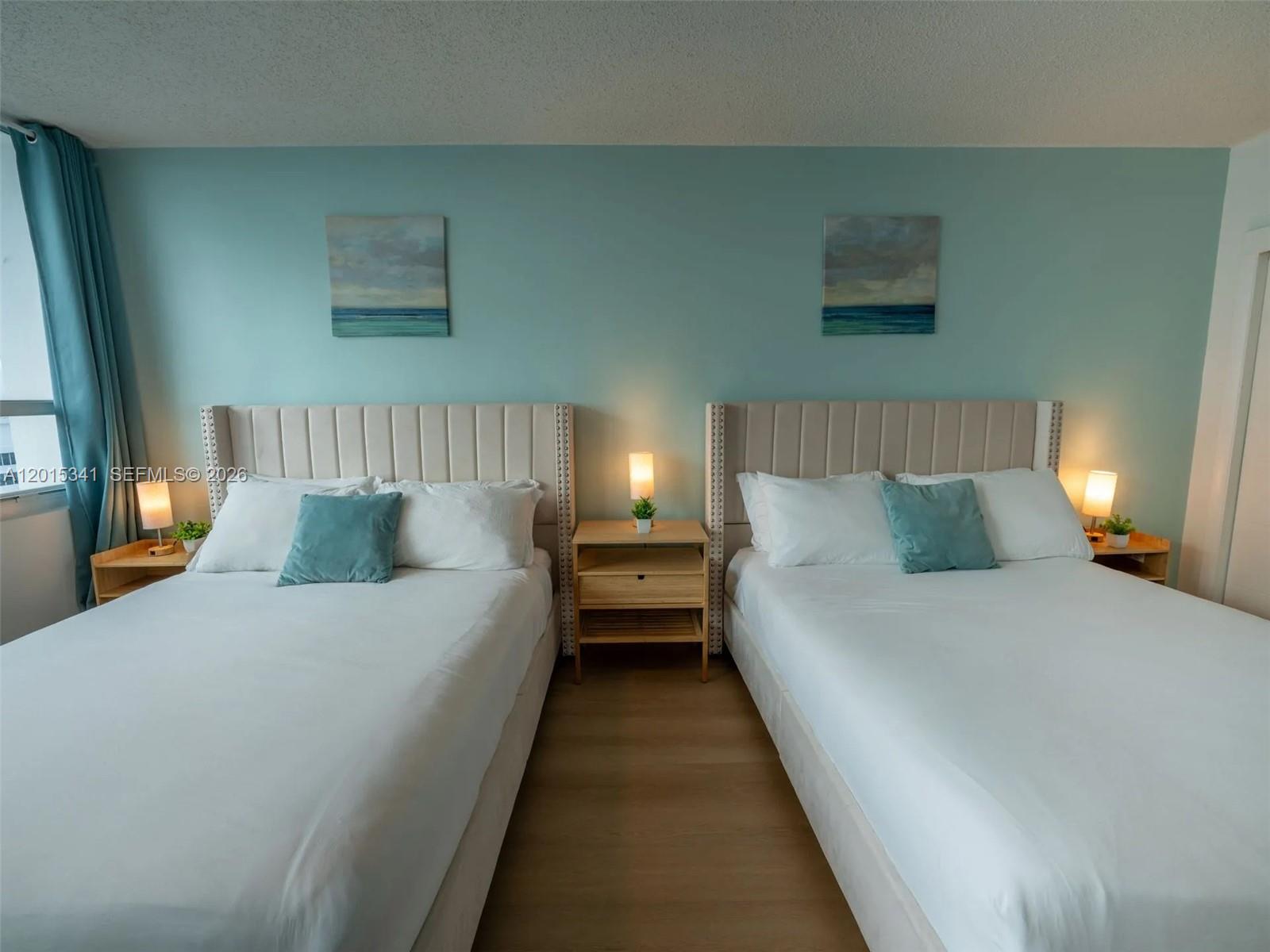 A bedroom features two beds with beige headboards, a shared nightstand, and light blue walls — 5445 Collins Ave # 1718, Miami Beach FL 33140, MIAMI BEACH, FL