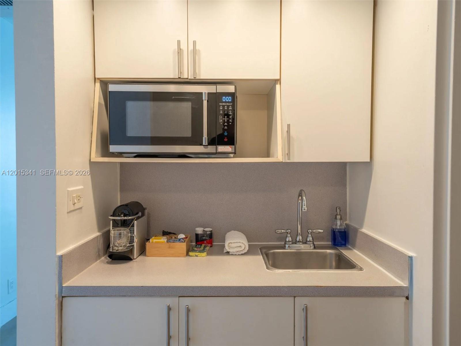 A small kitchenette features a stainless steel sink, microwave, and light-colored cabinetry — 5445 Collins Ave # 1718, Miami Beach FL 33140, MIAMI BEACH, FL
