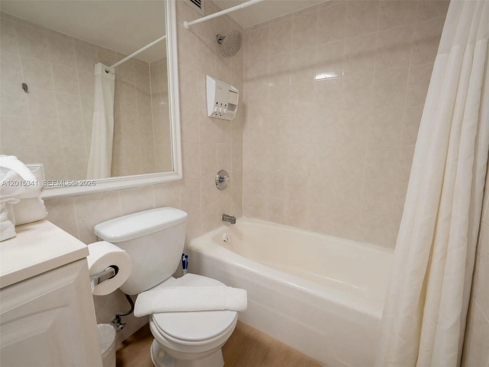 A bathroom features a white toilet, a bathtub with a shower head, and a vanity — 5445 Collins Ave # 1718, Miami Beach FL 33140, MIAMI BEACH, FL