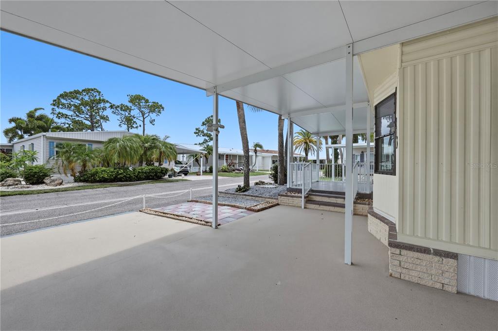 A covered carport area with concrete flooring leads to a small porch and stairs — 2100 KINGS HIGHWAY UNIT 835, PORT CHARLOTTE, FL