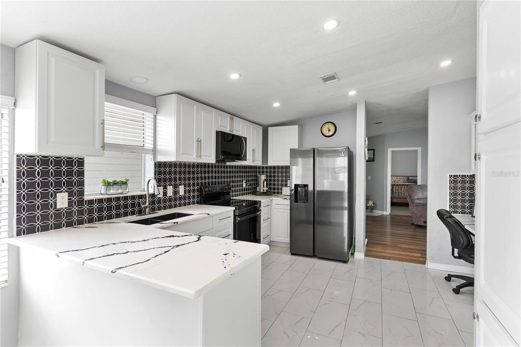 A modern kitchen features white cabinets, black patterned tile backsplashes, and white marble-look countertops — 9426 STAR GAZER LANE, RIVERVIEW, FL