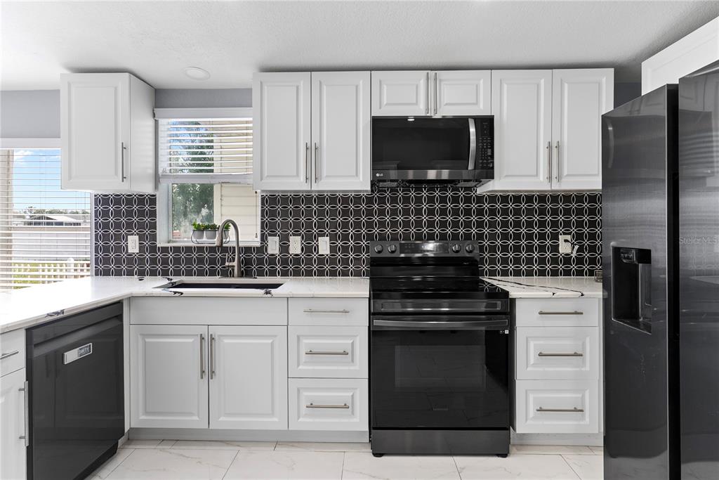 A kitchen features white cabinets, a black stove, a black refrigerator, and a patterned backsplash — 9426 STAR GAZER LANE, RIVERVIEW, FL