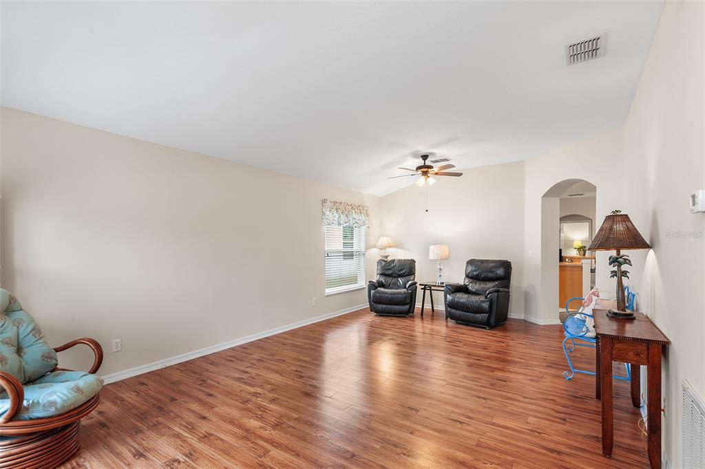 A living room features wood-look flooring, beige walls, a ceiling fan, and three armchairs — 4134 BEDFORD AVENUE, WINTER HAVEN, FL