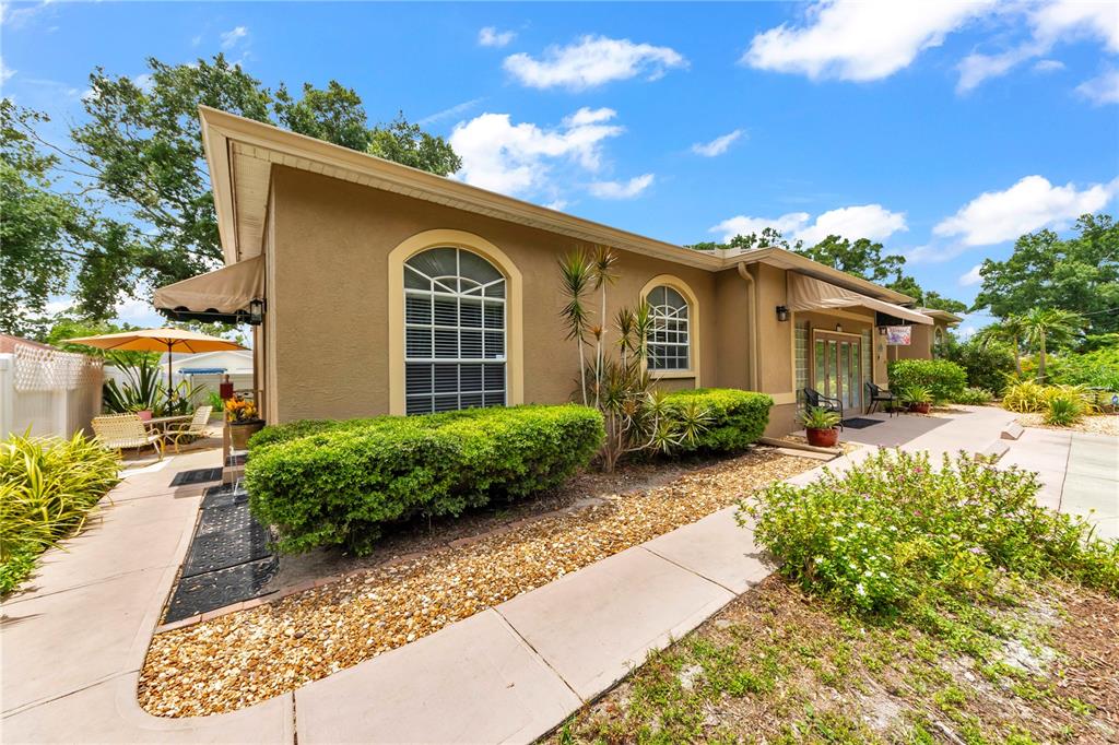 The exterior of a tan stucco house features arched windows, a patio, and landscaping — 7816 MARIGOLD AVENUE, TAMPA, FL