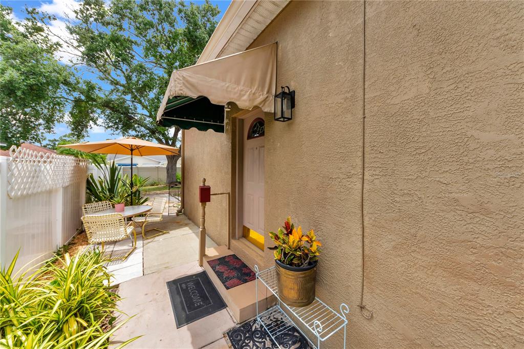 A tan stucco exterior wall features a doorway with a fabric awning and patio furniture — 7816 MARIGOLD AVENUE, TAMPA, FL