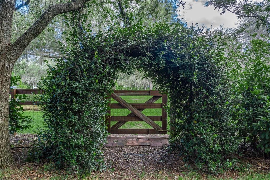 A wooden gate sits beneath a lush, arched hedge in a grassy outdoor area — 1273 SCRUB JAY TRAIL, FROSTPROOF, FL