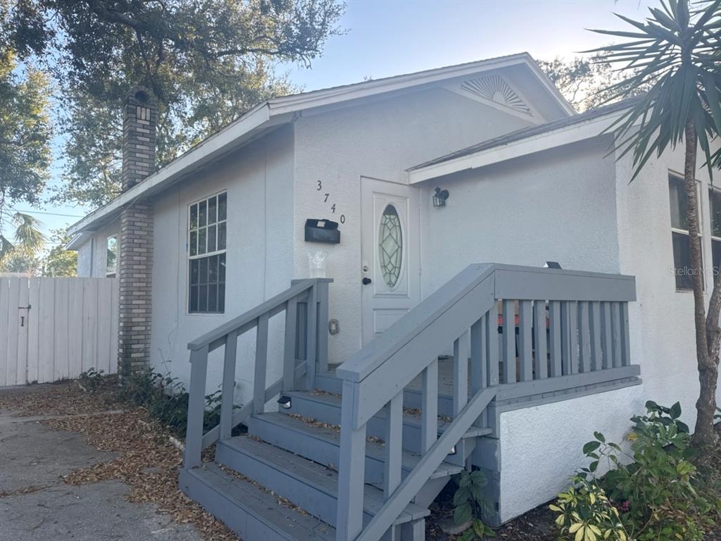 A small, light-colored house features a wooden staircase leading to a white front door — 3740 28TH AVENUE S, ST PETERSBURG, FL