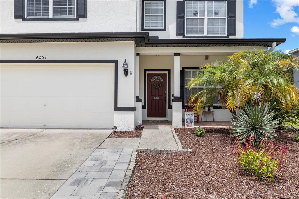 A two-story house exterior features a white stucco facade, a garage, and a front porch — 6053 EVERLASTING PLACE, LAND O LAKES, FL