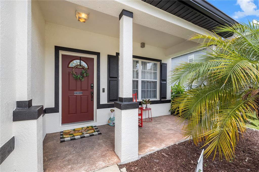 A covered front porch features a red door, a palm tree, and a concrete floor — 6053 EVERLASTING PLACE, LAND O LAKES, FL