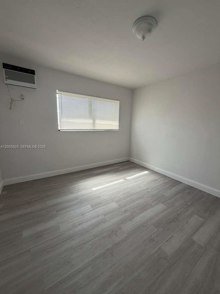 An empty bedroom features light gray wood-look flooring, white walls, a window with blinds, and an air conditioner — 1628 SW 7th St # 9, Miami FL 33135, MIAMI, FL