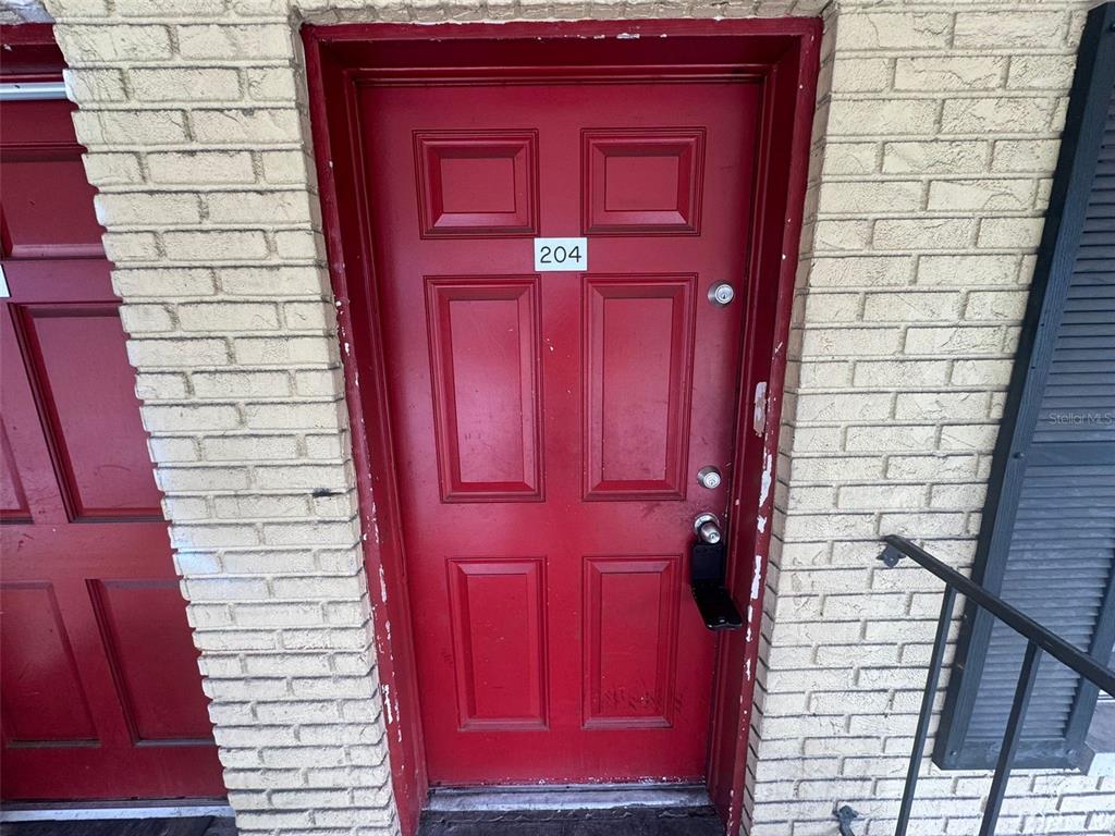 A red entry door with the number 204 is set into a light-colored brick wall — 2800 E 113TH AVENUE UNIT B1204, TAMPA, FL