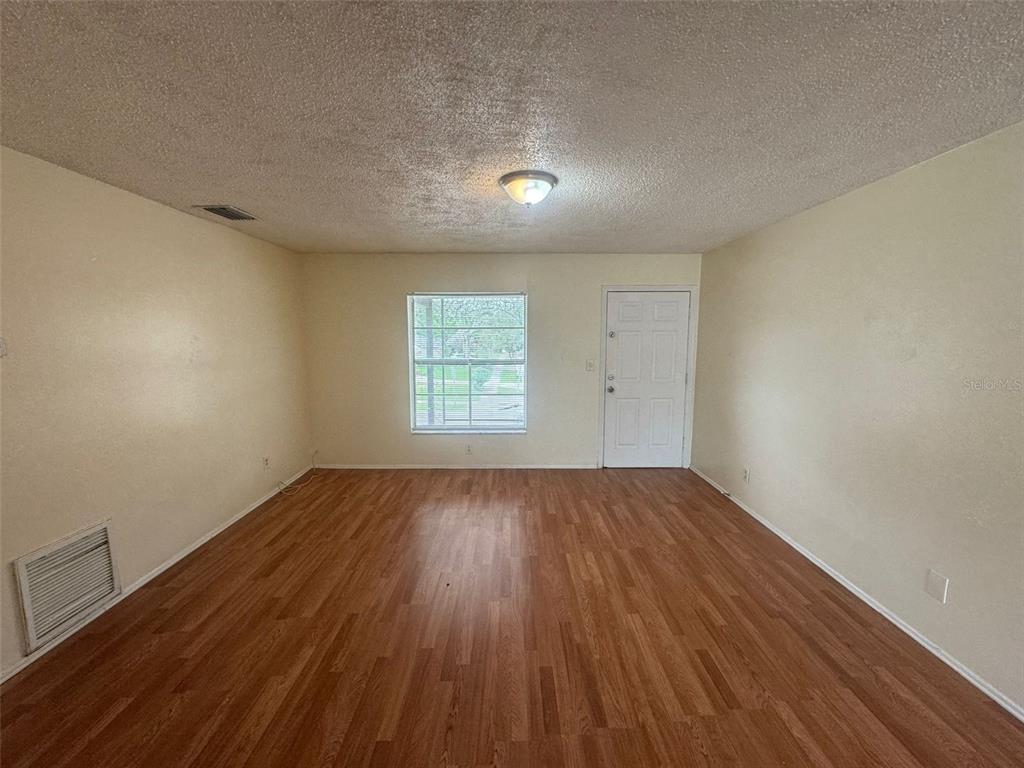 An empty room features light-colored walls, wood-look flooring, a single window, and a white door — 2800 E 113TH AVENUE UNIT B1204, TAMPA, FL