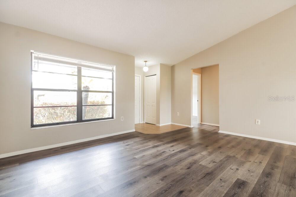 An empty living room features light beige walls, wood-look flooring, and a large window — 2225 HIDDEN MEADOWS DRIVE E, PALM HARBOR, FL