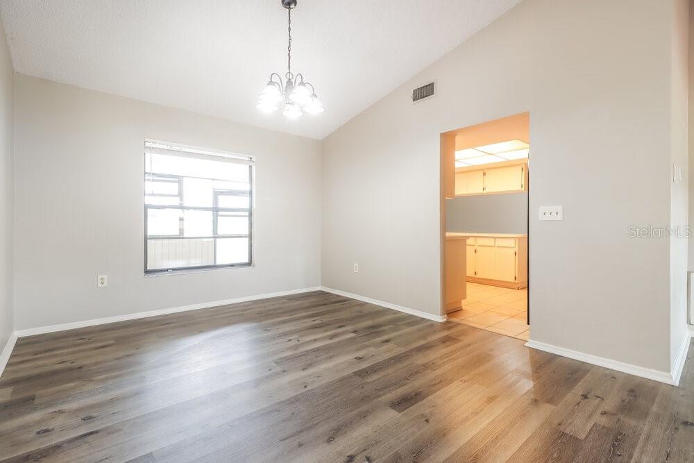 An empty dining room features light gray walls, wood-look flooring, and a vaulted ceiling — 2225 HIDDEN MEADOWS DRIVE E, PALM HARBOR, FL