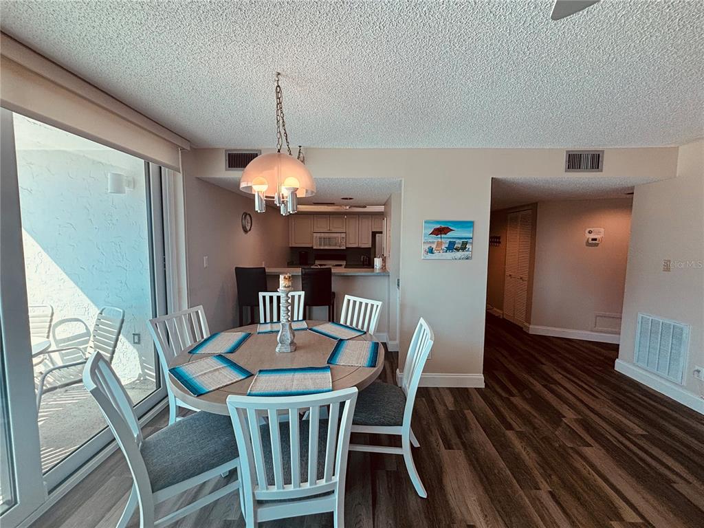 A dining area with a round table and chairs sits adjacent to a kitchen and balcony — 6518 MIDNIGHT PASS ROAD UNIT 209, SARASOTA, FL