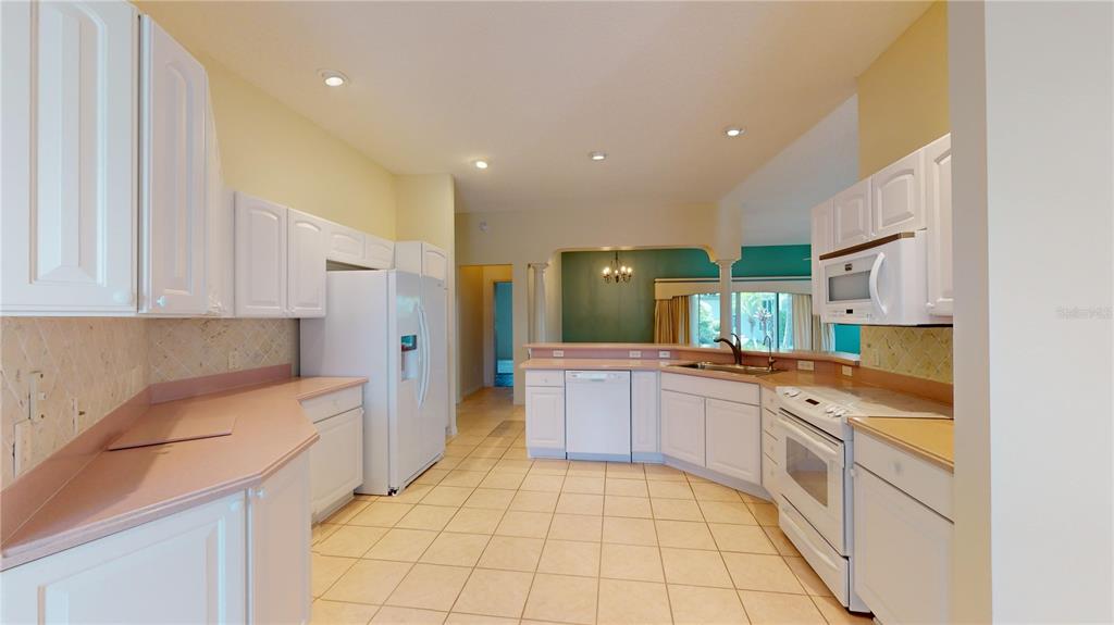 A kitchen with white cabinets, pink countertops, tile flooring, and a white appliance suite — 2613 AYALA WAY, THE VILLAGES, FL