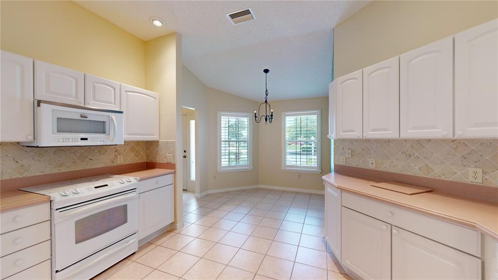 A kitchen with white cabinets, light countertops, tile backsplash, and an adjacent dining area — 2613 AYALA WAY, THE VILLAGES, FL