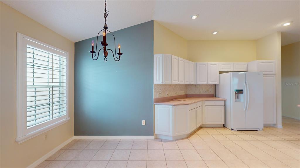 A kitchen and dining area with white cabinets, pink countertops, and a blue accent wall — 2613 AYALA WAY, THE VILLAGES, FL