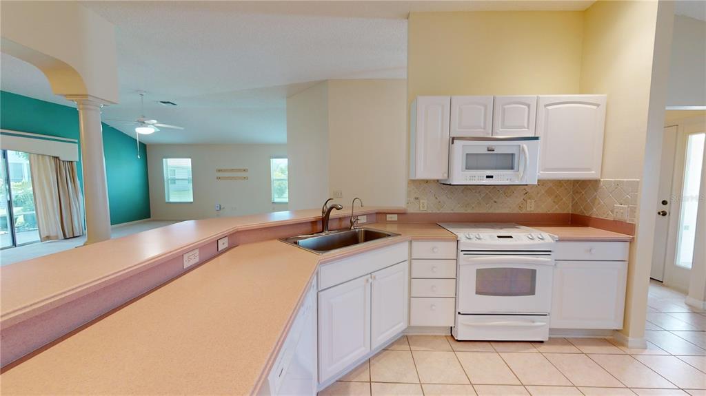 A kitchen features white cabinets, a light-colored countertop, and a white stove and microwave — 2613 AYALA WAY, THE VILLAGES, FL