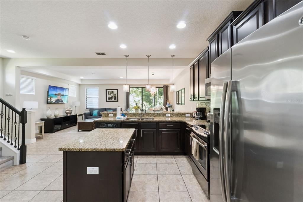A kitchen with dark wood cabinets and granite countertops overlooks an open-concept living area — 8137 ROSEVILLE ROAD, DAVENPORT, FL