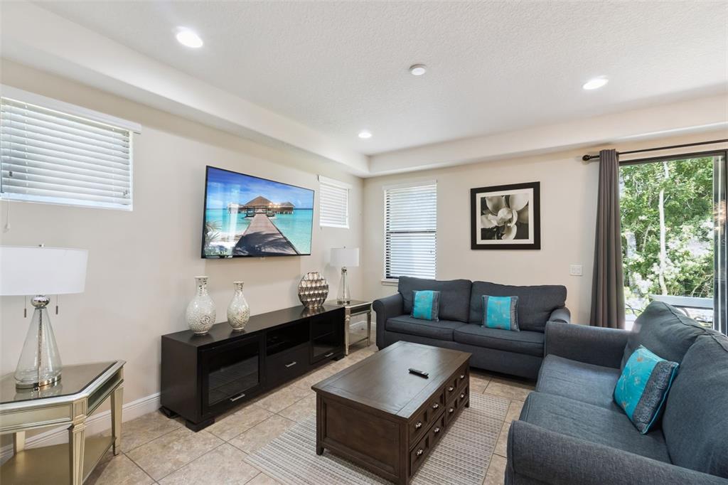 A living room features a wall-mounted television, dark furniture, blue sofas, and tile flooring — 8137 ROSEVILLE ROAD, DAVENPORT, FL