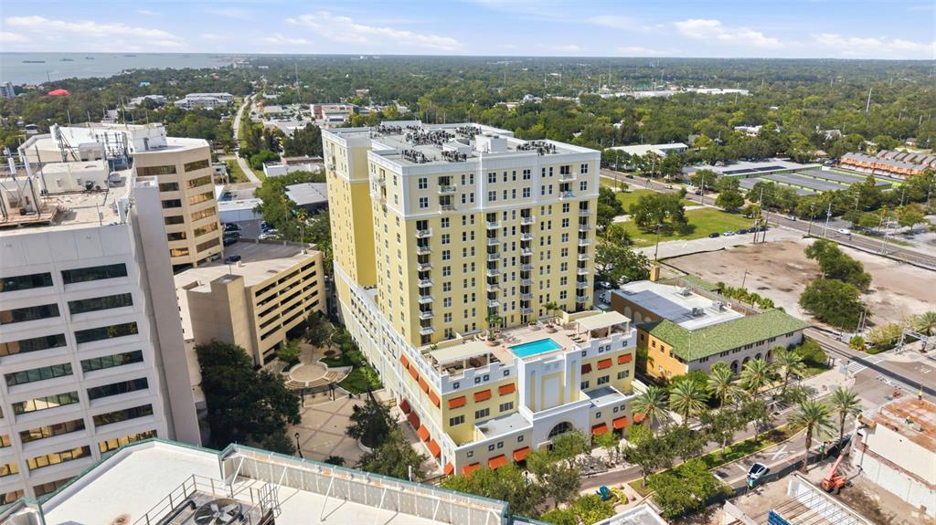 An aerial view shows a tall yellow apartment building with a rooftop pool and parking garage — 628 CLEVELAND STREET UNIT 1211, CLEARWATER, FL