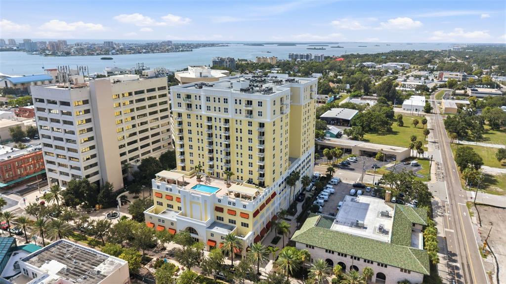 An aerial view shows a tall yellow apartment building with a rooftop pool and surrounding cityscape — 628 CLEVELAND STREET UNIT 1211, CLEARWATER, FL
