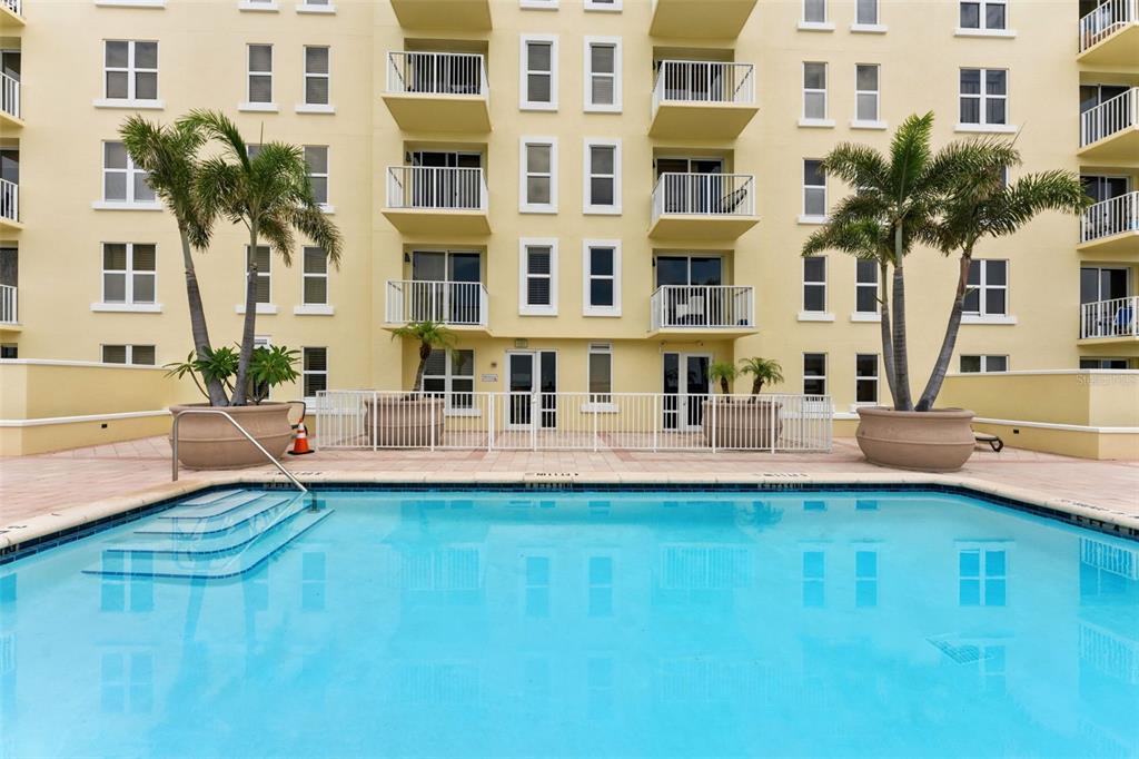 A swimming pool sits in front of a multi-story apartment building with balconies and palms — 628 CLEVELAND STREET UNIT 1211, CLEARWATER, FL